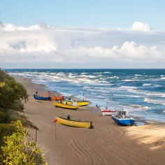 Plaża nad Bałtykiem z kolorowymi łodziami rybackimi i falującym morzem.