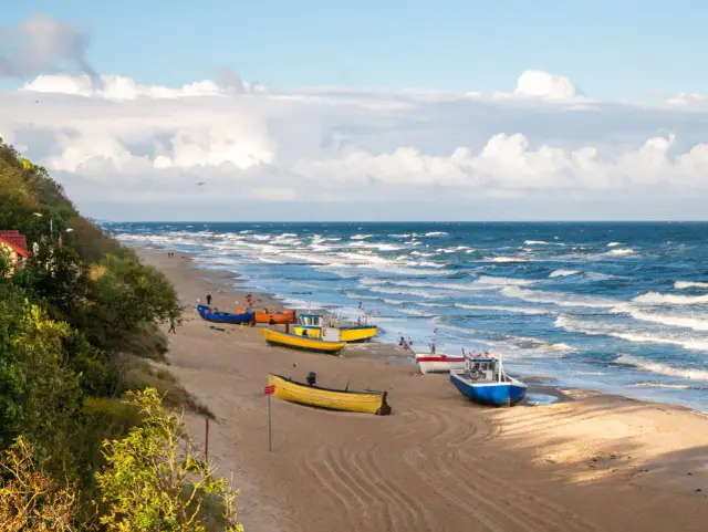 Plaża nad Bałtykiem z kolorowymi łodziami rybackimi i falującym morzem.